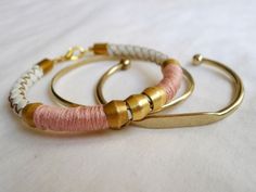 two bracelets with gold and pink thread on them sitting on a white cloth covered surface