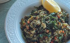 a white bowl filled with rice and vegetables next to a lemon wedge on top of a table