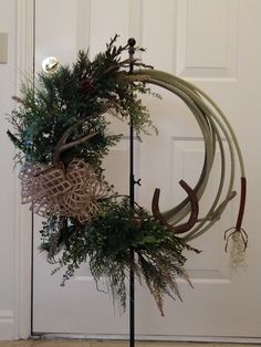 a wreath with antlers and pine needles hanging on a pole in front of a door