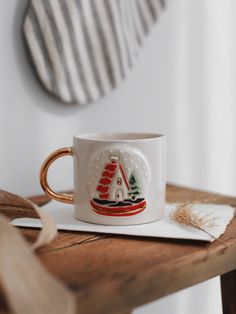 a coffee cup with a sailboat on it sitting on a wooden table next to a mirror