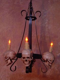 a chandelier with three skulls hanging from it's sides and two candles in the middle