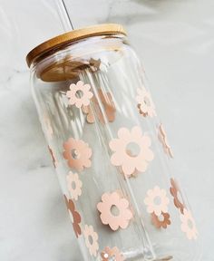 a mason jar with pink and gold flowers on the lid sitting on a marble surface