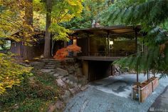 a house in the woods surrounded by trees and rocks, with a stone walkway leading up to it