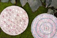 two circular mosaics sitting on top of green grass next to leaves and plants in the background