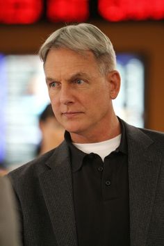 a man with grey hair wearing a black suit and white t - shirt looking at the camera