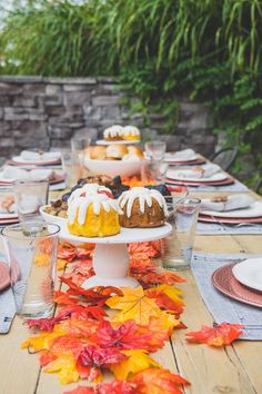 a wooden table topped with lots of plates and cups filled with dessert covered in frosting