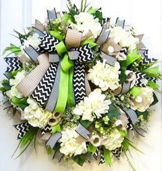 a wreath with white flowers and green ribbon hanging on a door handle that is decorated with black and white chevron ribbons