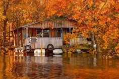 an old boathouse is surrounded by water and trees with orange leaves on the ground