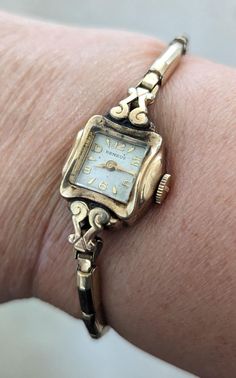 "This is a gorgeous Benrus 10K yellow rolled gold plated ladies watch that is currently NON working. I am not a watch expert, nor have I had it tested or serviced, it is being sold AS IS.  The face is a square with a pearly ivory face and gold hands and numerals. There is a lovely scroll design around the watch face that really sets it apart. The watch is marked 10k RGP on the back. This watch is approximately 6\". The band is a vintage segmented stretch band that also has a lot of visual interest in that it has an irregular shape.  This bracelet makes a statement and are perfect for anyone who loves vintage or steampunk style. Wear one on its own for a simple and elegant look, or pair with one of my necklaces and earrings to create a bold and eye catching outfit. Add a touch of time-worn Luxury Antique Gold Watch Bands, Luxury Vintage Rectangular Watch Accessories, Luxury Vintage Watch Accessories For Anniversary, Luxury Antique Watches With Subdials, Luxury Vintage Watch For Anniversary, Luxury Vintage Watch Bracelet Strap, Victorian Yellow Gold Watches For Anniversary, Victorian Yellow Gold Anniversary Watch, Antique Hallmarked Watches For Wedding