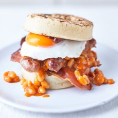 an egg and bacon sandwich is on a white plate with some corn kernels around it