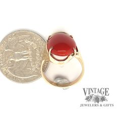 This modern 14 karat yellow gold design holds an oval cabochon of increasingly rare red coral. The natural coral has a vibrant red color with little to no mottling. The coral displays even color with slight growth lines near a prong. The ring is a semi free form design with the mounting offering support to the coral. The stone is secured with 4 prongs and is size 7. Red Cabochon Ruby Ring In 14k Gold, 14k Gold Red Cabochon Ruby Ring, Oval Cabochon Red Ruby Ring In 14k Gold, Red Ruby Oval Cabochon Ring In 14k Gold, Red Domed Gemstone Rings, Yellow Gold Carnelian Oval Cabochon Ring, Classic Red Oval Cabochon Signet Ring, Yellow Gold Oval Cabochon Carnelian Rings, Carnelian Yellow Gold Rings With Oval Cabochon