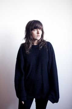 a woman standing in front of a white wall with her hands on her hips and looking off to the side