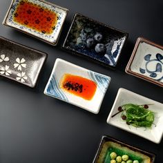 nine small plates with different types of food in them on a black surface, one has blueberries and the other is orange