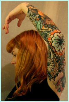 a woman with red hair and tattoos on her arm pointing at the camera while she holds her hand up in front of her head