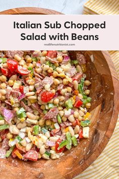 a wooden bowl filled with salad and beans on top of a striped table cloth next to a