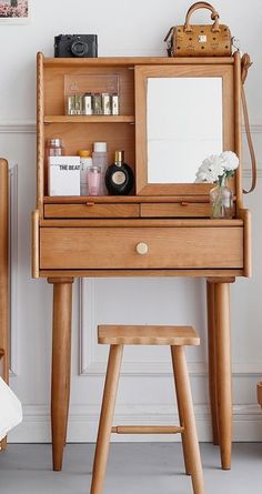 a wooden desk with a mirror, stool and other items on it in front of a white wall