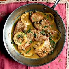 a pan filled with meat and lemons on top of a pink table cloth next to a fork