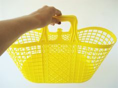 a hand holding a yellow plastic basket over a white background with the handle extended up