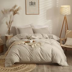 a bed with white sheets and pillows in a room next to a chair, lamp and pictures on the wall