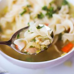 a close up of a spoon full of soup with noodles and carrots in it