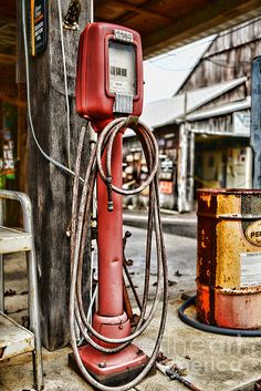 an old red gas pump sitting on the side of a road next to a pole