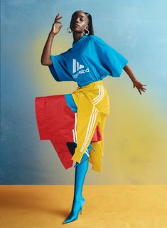 a woman in blue shirt and yellow skirt standing on one leg with her arms out