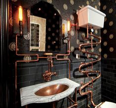 a bathroom with black and gold wallpaper, copper pipes, white sink and toilet