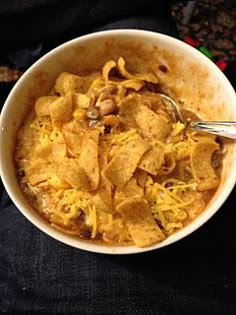 a white bowl filled with food on top of a black cloth covered table next to a spoon