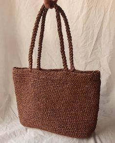 a brown straw bag on a white sheet with a hand holding it up to the side