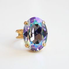 This stunning crystal cocktail ring is sure to turn heads! A gorgeous 18mm oval crystal is set in a luxurious, adjustable gold plated (or silver) ring band that can fit sizes 5 and up. This 12-carat gem is perfect for any special occasion or for adding an eye-catching sparkle to your everyday look. As the light catches it, the crystal gleams in shades of purple, blue and green. Plus, the ring base is Nickel free! Ships Free • Handmade in the USA Gold Filigree Earrings, Crystal Rainbow, Crystal Teardrop Earrings, Swarovski Crystal Rings, Swarovski Ring, Rose Gold Earrings Studs, Clear Earrings, Gold Bridal Earrings, Ring Crystal