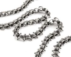 a silver chain with spikes on it is laying on a white surface and there are other chains in the background