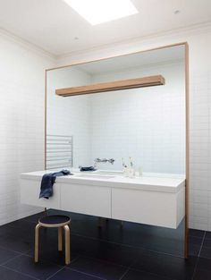 a white bathroom with black tile flooring and a large mirror over the sink that's mounted to the wall