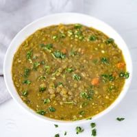 a white bowl filled with green lentula soup on top of a white tablecloth