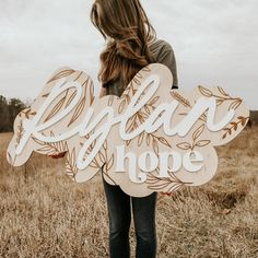 a woman standing in a field holding a wooden sign that says, right now hope