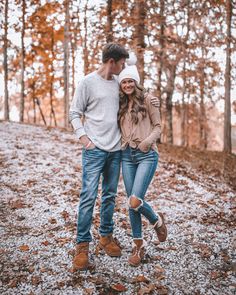 a man and woman are standing in the woods with leaves on the ground around them