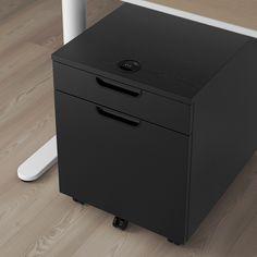 a black filing cabinet sitting on top of a hard wood floor next to a computer desk