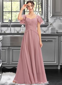 a woman in a long pink dress standing next to a kitchen sink and stove top