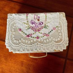 a white doily with pink flowers on it sitting on top of a wooden table