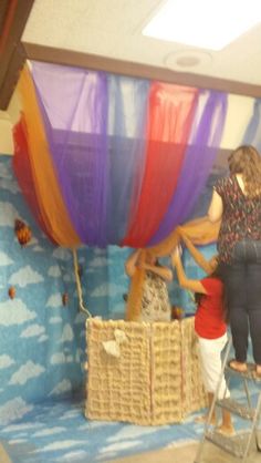 two women working on a large balloon in a room with blue and white walls,