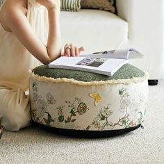 a woman sitting on the floor next to a flower covered ottoman and reading a book