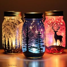 three mason jars with painted deer and pine trees on them, sitting on a table