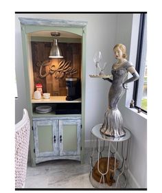 a statue is holding a wine glass in front of a cabinet with an open door