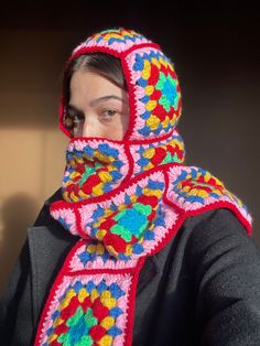 a woman wearing a colorful crocheted scarf with a hood on her head and neck