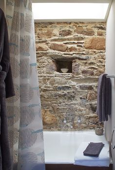 a bathroom with stone walls and a bathtub next to a shower curtain that is open