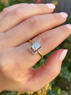 a woman's hand holding a ring with an emerald stone in the middle and diamonds around it