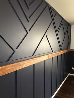 an empty room with black painted walls and wood flooring on the wall, along with a wooden shelf