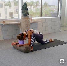 a woman is doing yoga in front of a window with a statue on the floor