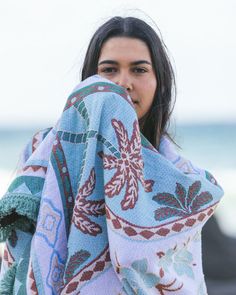 a woman wrapped in a blanket on the beach with her hand under her face and looking at the camera