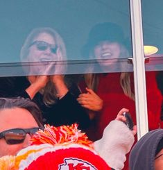 two women and a man in the stands at a football game with their cell phones up to their ear