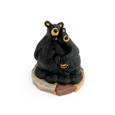 two black bears sitting next to each other on top of a piece of wood with yellow eyes